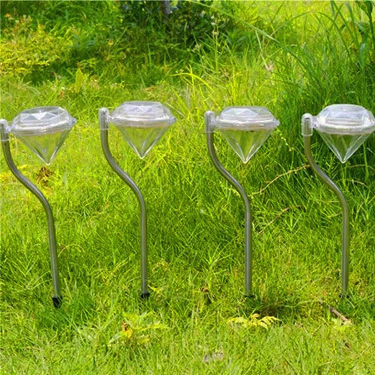 Four diamond-shaped solar lights with silver stems stand in a lush green grassy area during the day.