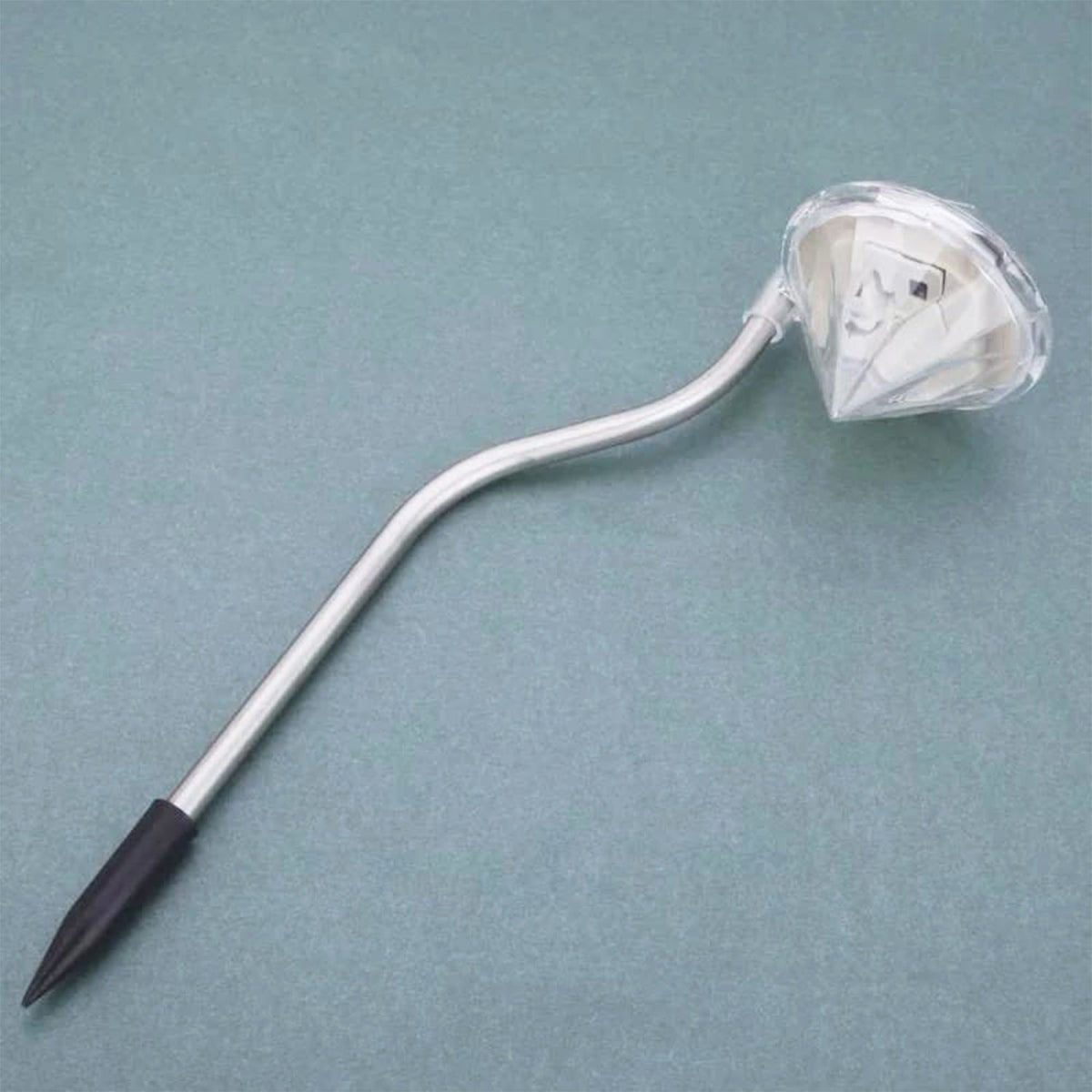 A single diamond-shaped solar light with a silver curved stem and black ground stake rests on a blue-grey surface.
