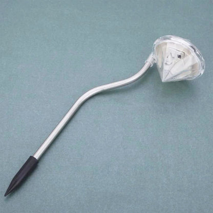 A single diamond-shaped solar light with a silver curved stem and black ground stake rests on a blue-grey surface.