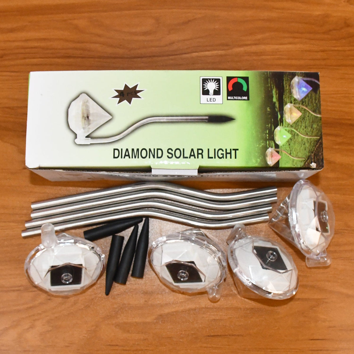 A box labeled "Diamond Solar Light" with illustrations, and four disassembled lights with stakes and stems on wood.