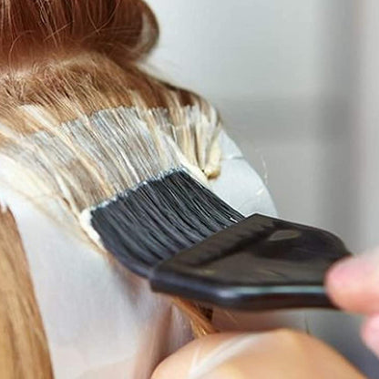 Close-up of a hand in a white glove applying white hair dye to light brown hair with a black brush.