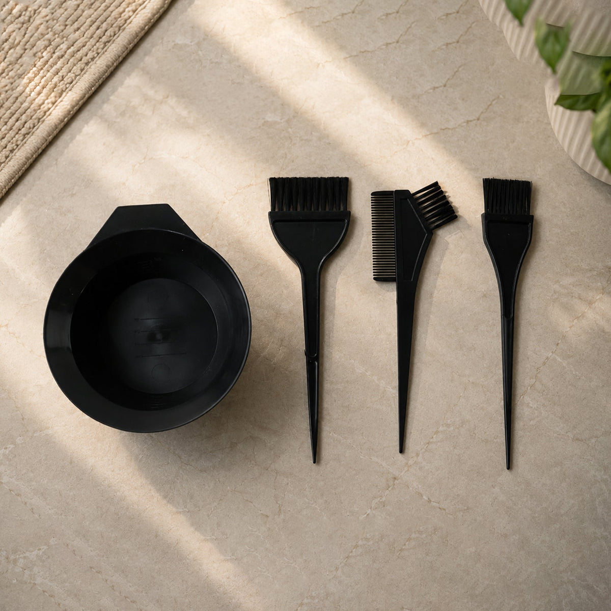A black hair dye kit, including a bowl and three brushes, arranged on a light grey textured surface.