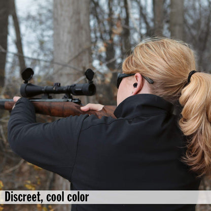 A woman with blonde hair in a ponytail aims a rifle, wearing a black earplug in her right ear.