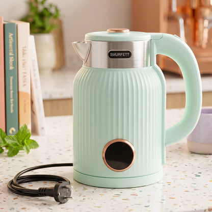 A person pours steaming water from a mint green electric kettle with a visible power button into a two-toned ceramic mug.