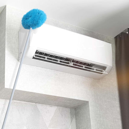 A blue microfiber duster on an extended handle is shown cleaning the top of a white wall-mounted air conditioner.
