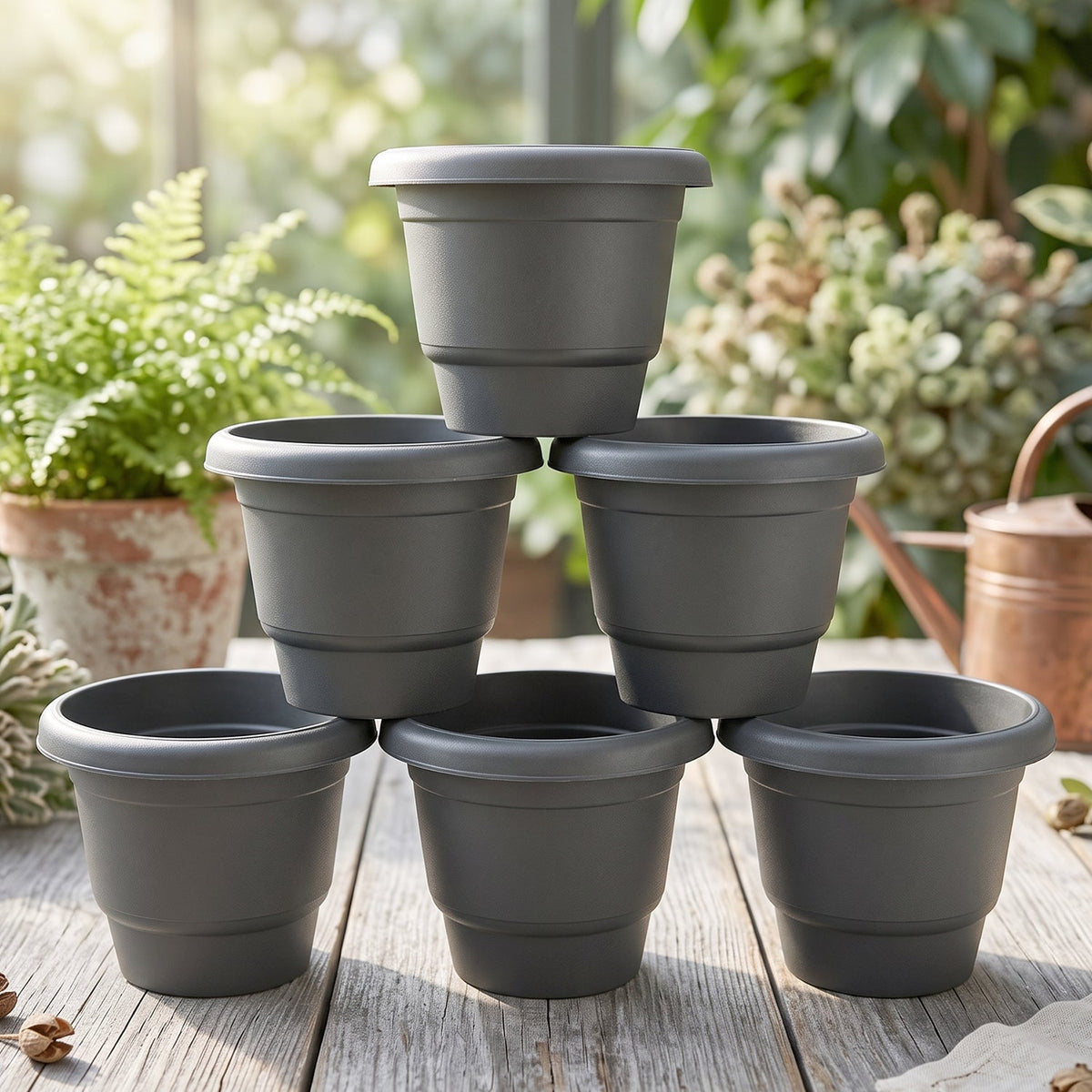 Six gray plastic flower pots stacked in a pyramid on a wooden table, with lush green plants blurred in the background.