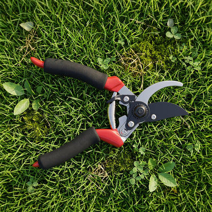 Red and black pruning shears lie open on vibrant green grass with small clover leaves.