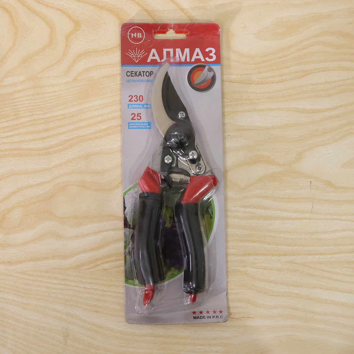 Red and black pruning shears are sealed in retail packaging, displayed on a light wooden surface.