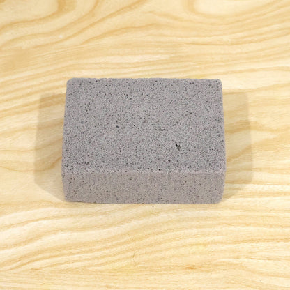 A single gray rectangular cleaning block with a porous texture centered on a light wooden surface.