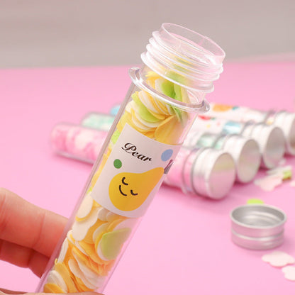 A hand holds an open clear tube of yellow and green flower-shaped paper soap strips with a pear label on a pink background.