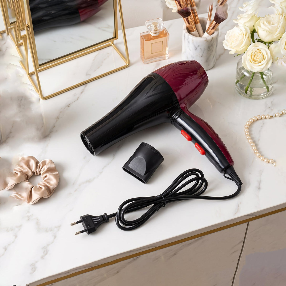 A red and black hair dryer with its concentrator nozzle and cord is arranged on a white marble vanity.