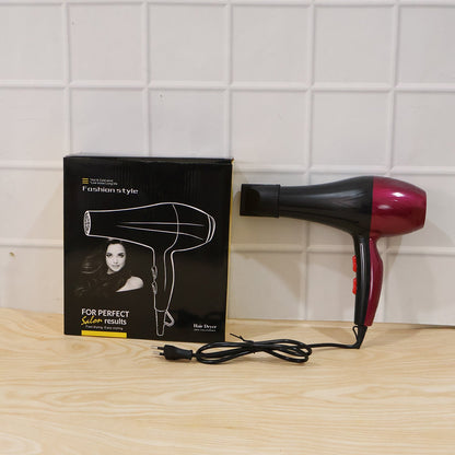 A red and black hair dryer with its black packaging box and power cord sits on a light wooden surface.