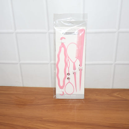 A clear plastic package containing four pink hair styling tools stands upright on a wooden surface against a white tiled