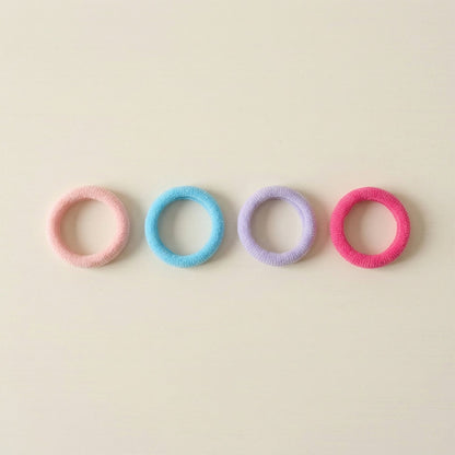 Four colorful elastic hair ties in pink, blue, lavender, and fuchsia arranged in a row on a light beige surface.
