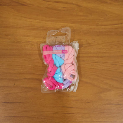 A clear plastic package containing 35 colorful elastic hair ties, including pink, blue, and lavender, on a wooden surface.
