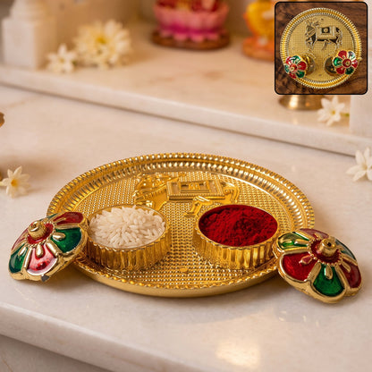 A golden pooja thali with a cow design, two small bowls of rice and kumkum, and two flower-shaped lids.