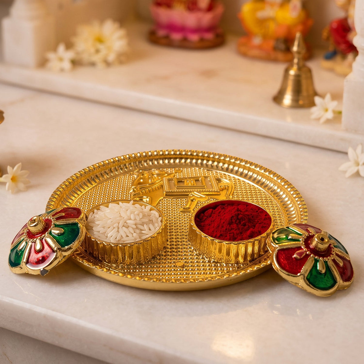 A golden pooja thali with a cow design, two small bowls of rice and kumkum, and two flower-shaped lids on a marble surface