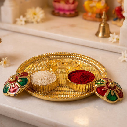 A golden pooja thali with a cow design, two small bowls of rice and kumkum, and two flower-shaped lids on a marble surface