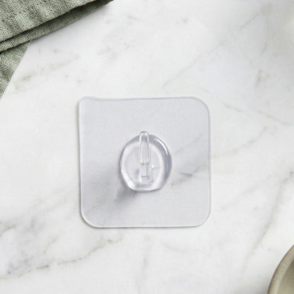 A clear self-adhesive wall hook centered on a light grey marble surface with a green cloth in the corner.
