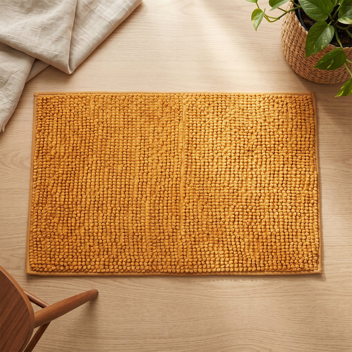 A rectangular mustard yellow bobble mat with a distinct central seam lies flat on a light wooden floor.