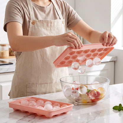 Person using a pink ice ball tray to add clear ice balls to a fruit-filled glass bowl.