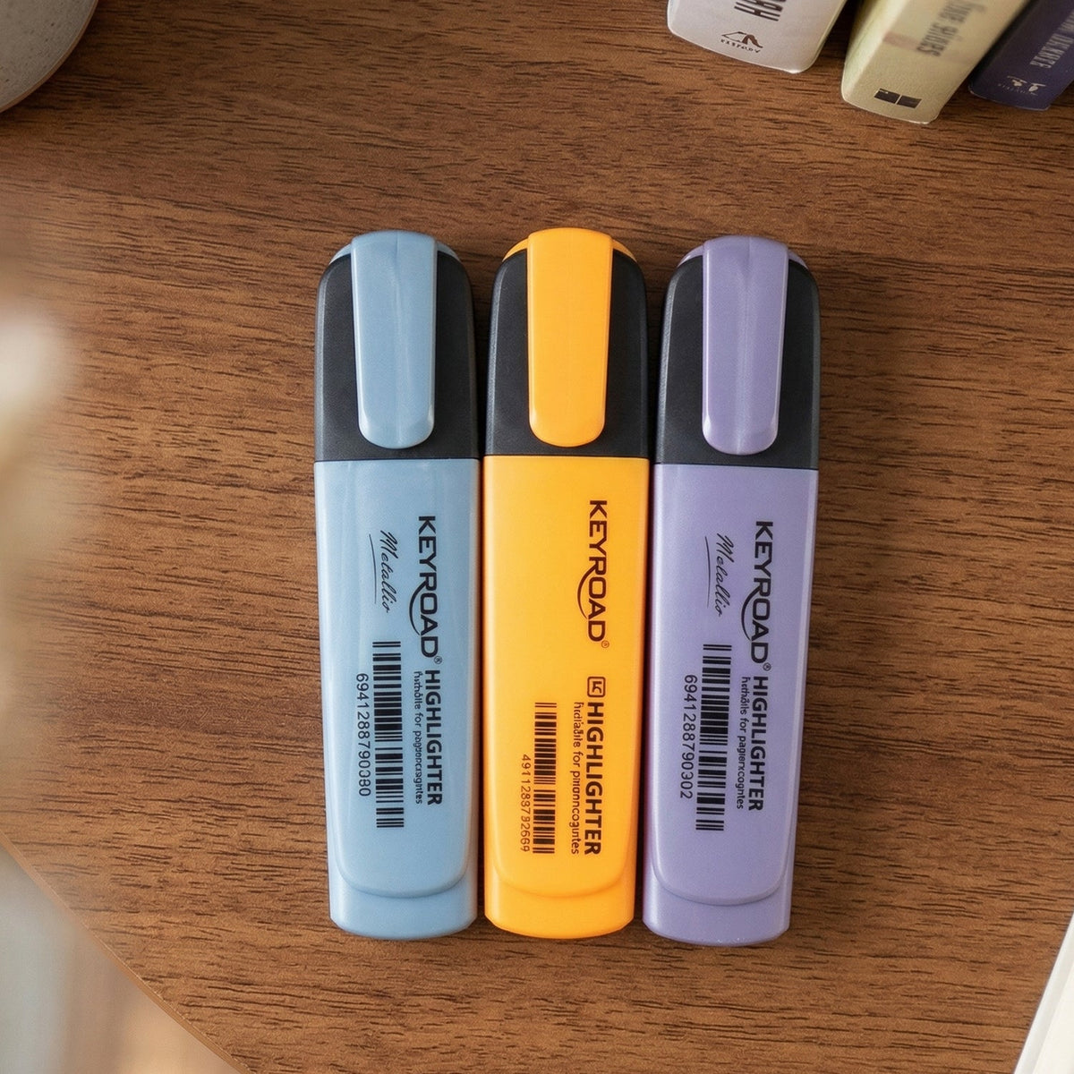 Three Keyroad Metallic highlighters in light blue, orange, and purple stand upright on a wooden surface.