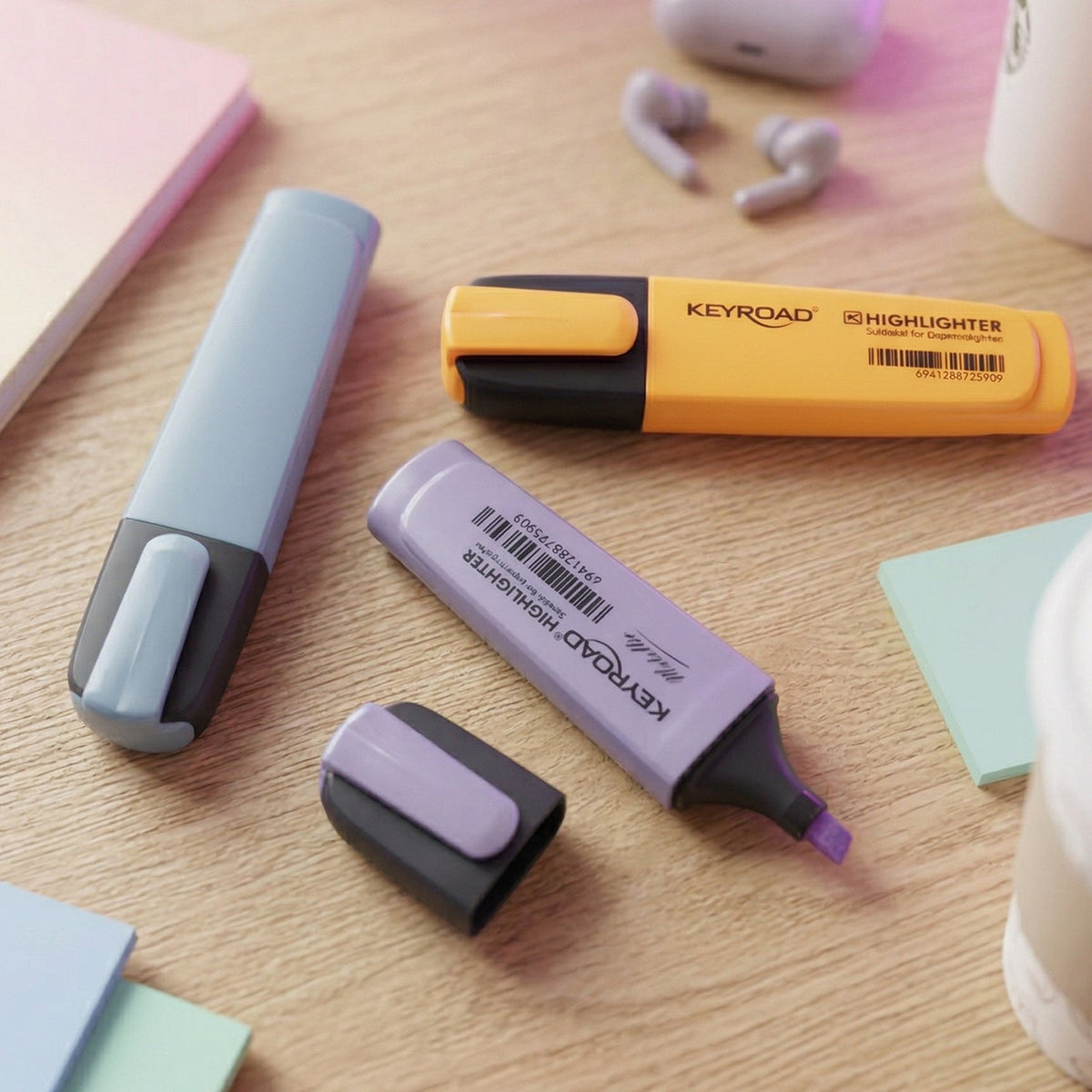 Three Keyroad Metallic highlighters in light blue, purple, and orange are arranged on a wooden desk with office supplies.