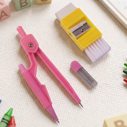 A pink compass, yellow eraser with brush, and lead refills on a white textured surface with colorful blocks.