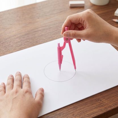 Hands using a pink compass to draw a circle on a white sheet of paper on a wooden desk.