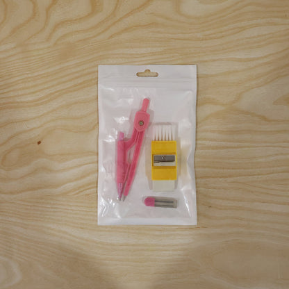 The pink compass, yellow eraser with brush, and lead refills are sealed in clear plastic packaging on a light wooden surface.