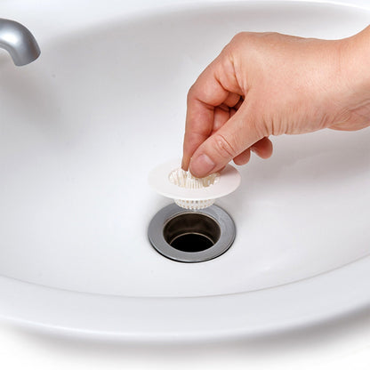 A hand holds a white plastic sink drain strainer above a sink's metal drain opening.