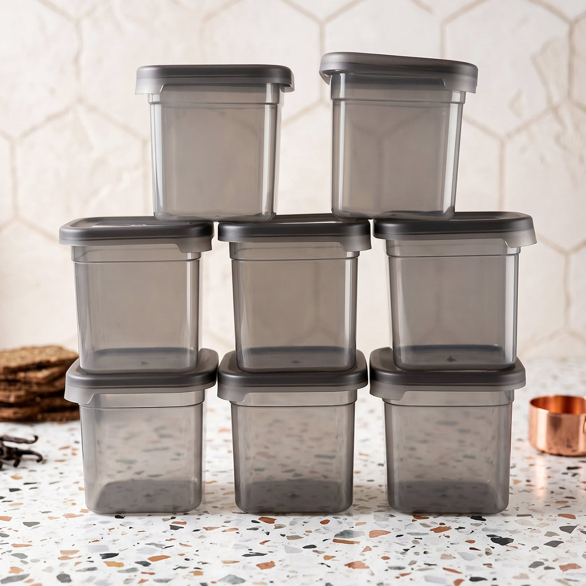 Eight empty, clear plastic food storage containers with gray lids, stacked on a speckled countertop with a copper cup.