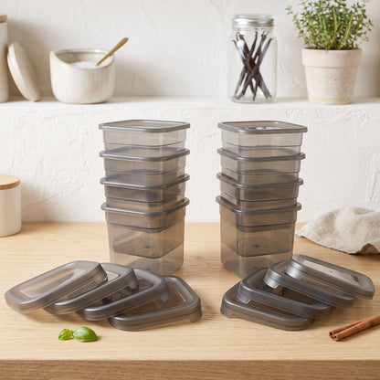 Two stacks of empty clear plastic containers and loose gray lids arranged on a light wooden surface with kitchen items.