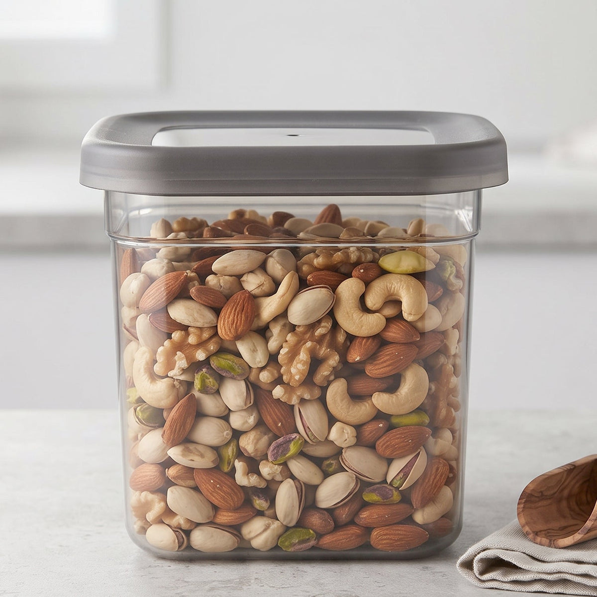 A single clear plastic food storage container with a gray lid, filled with a colorful mix of nuts and seeds.