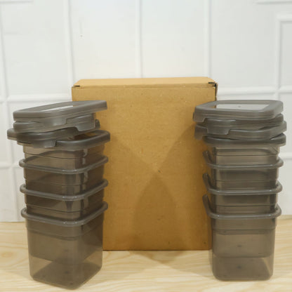Two stacks of empty clear plastic food containers with gray lids, flanking a brown cardboard box on a wooden surface.