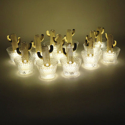 Twelve gold cactus LED tealights with clear textured bases emit a warm glow in a dimly lit setting.