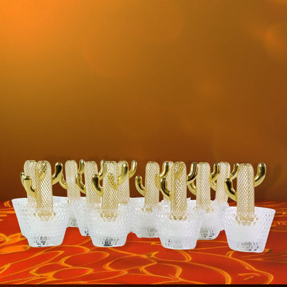 Twelve gold cactus LED tealights with clear bases glow on a red and orange patterned surface against an orange wall.