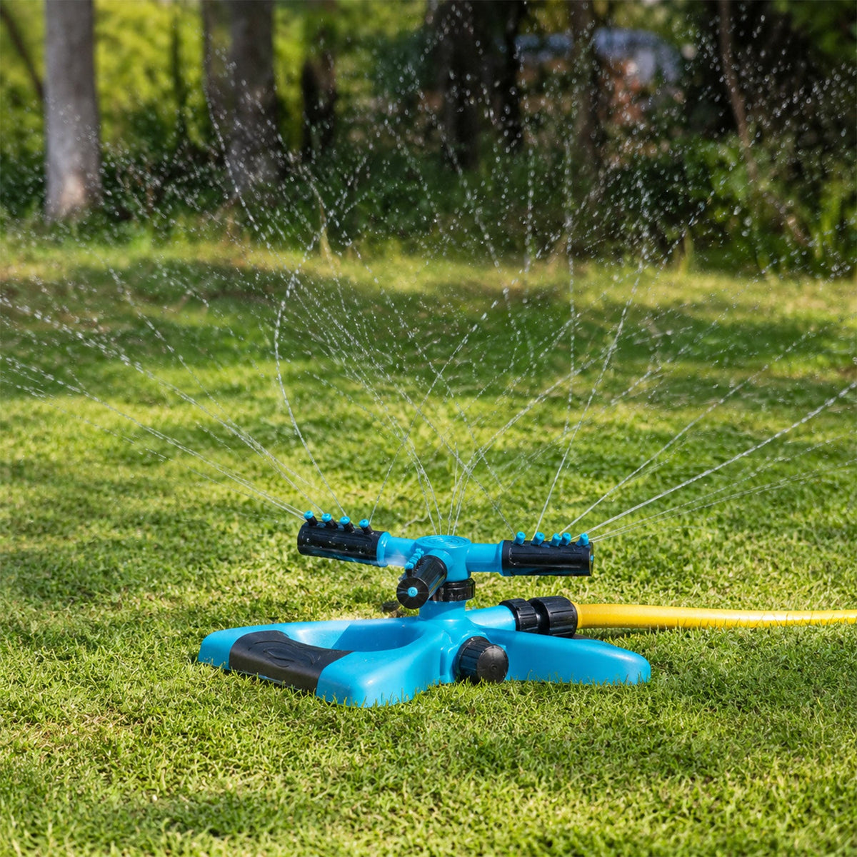 A blue and black sprinkler with a yellow hose attached, actively spraying water across a vibrant green lawn.