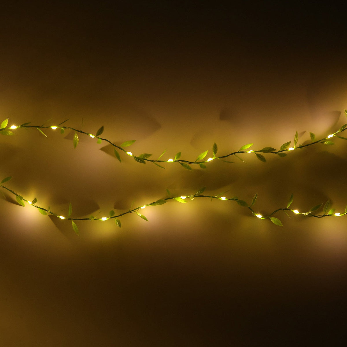 Two horizontal strands of green leaf string lights with small, warm white LEDs against a dark background.