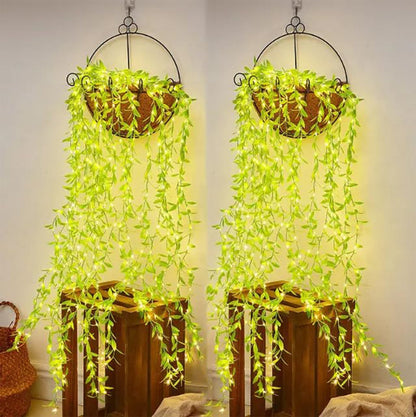 Two identical hanging baskets with long strands of green leaf string lights cascading over wooden crates against a light