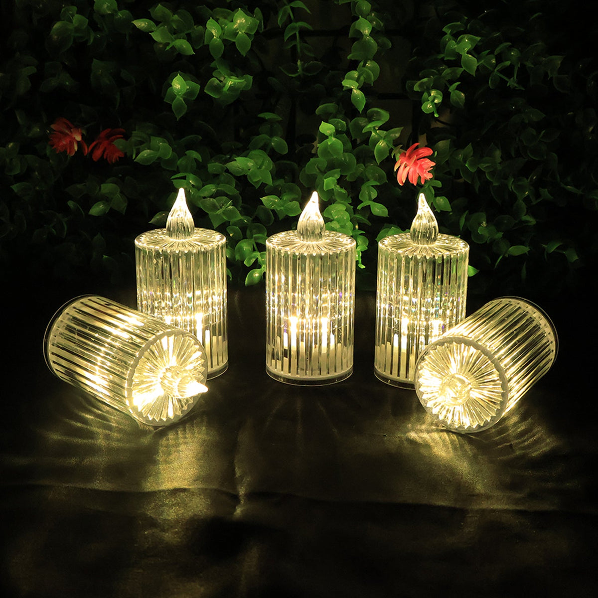 Five clear ribbed LED flameless candles with warm glow, three upright and two lying on their sides, against a green