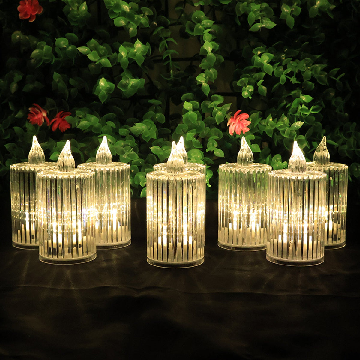 Eight clear ribbed LED flameless candles with warm glow arranged in two rows against a green leafy background.
