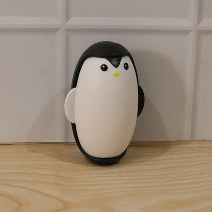 A black and white penguin lint roller stands upright on a light wooden surface against a white tiled wall.