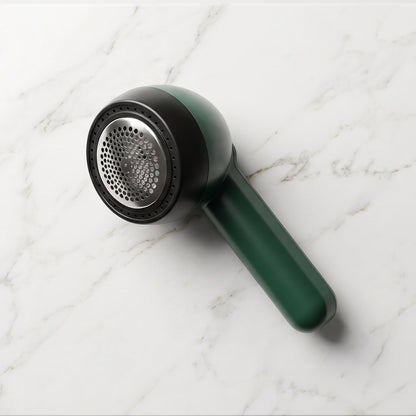 A dark green and black lint remover with a silver mesh head rests on a white marble surface.