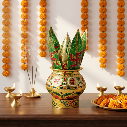 A golden metal Kalash with green leaves, incense, and lamps on a wooden surface.