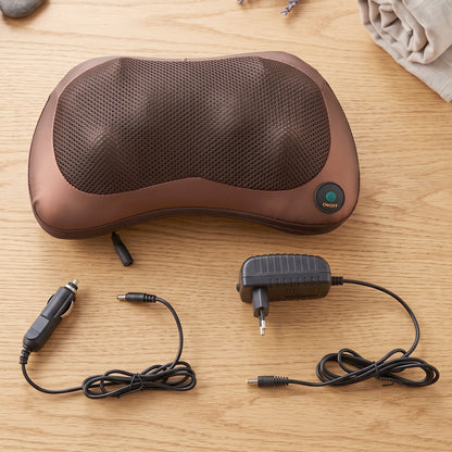 A brown massage pillow with its car charger and wall adapter displayed on a wooden surface next to a rolled towel.
