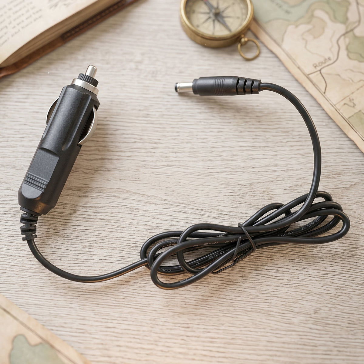 A black car charger cable with a DC barrel jack connector on a wooden surface with a compass and book.