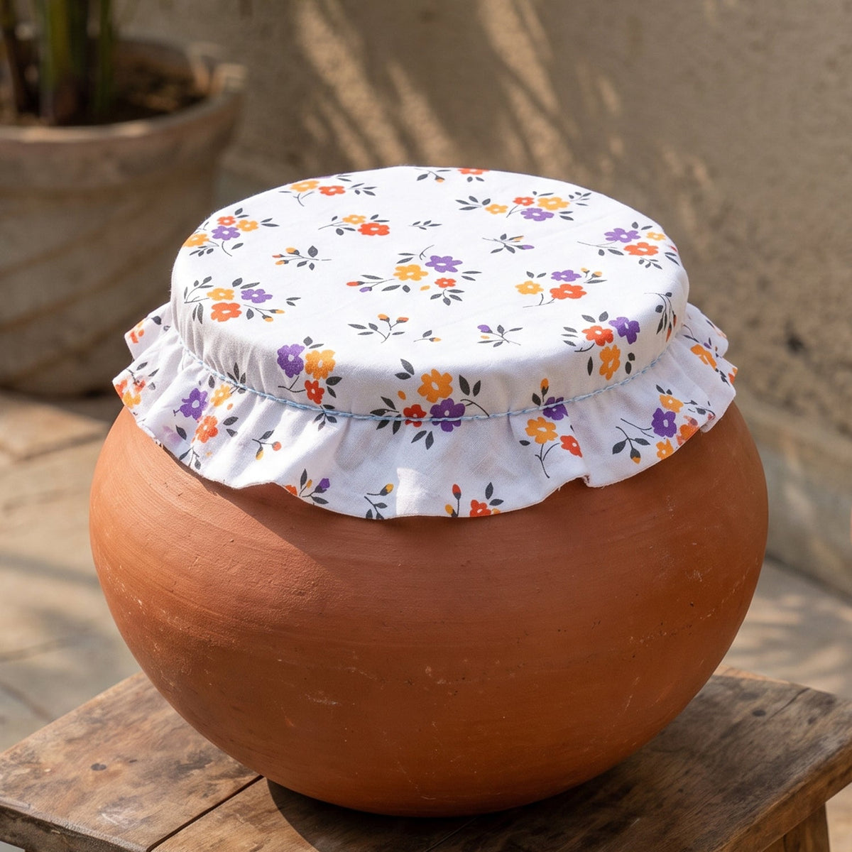 Overhead view of a white floral food cover on a terracotta water pot outside.