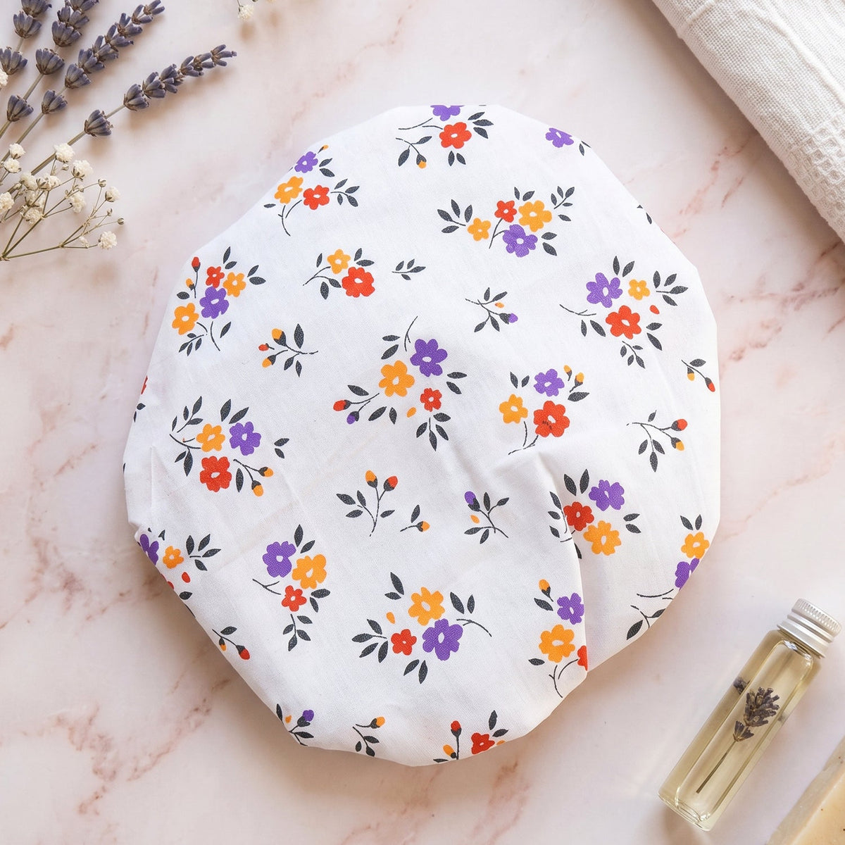 Floral patterned food cover on a marble surface with lavender sprigs and small oil bottle.