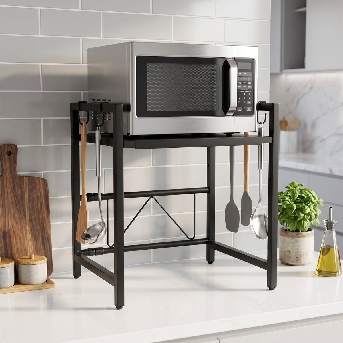 Stainless steel microwave on a black metal rack with kitchen utensils hanging, against a gray tiled wall.